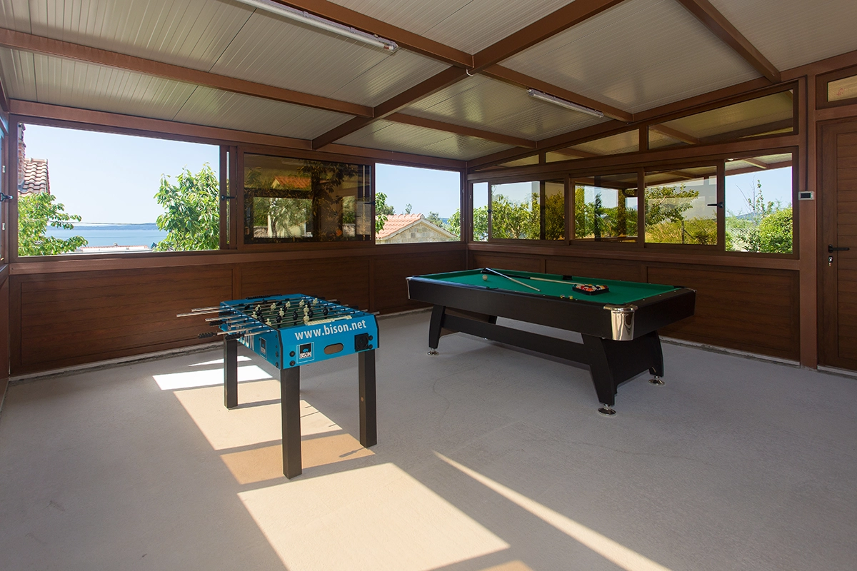 Enclosed outdoor wooden space designed for entertainment, equipped with a dartboard, foosball table, and billiards.